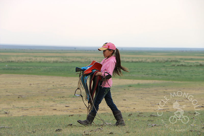 Herder girl carrying saddle to her horse