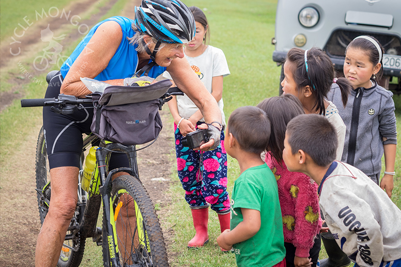 A rider is being greeted by local children cycling through steppe